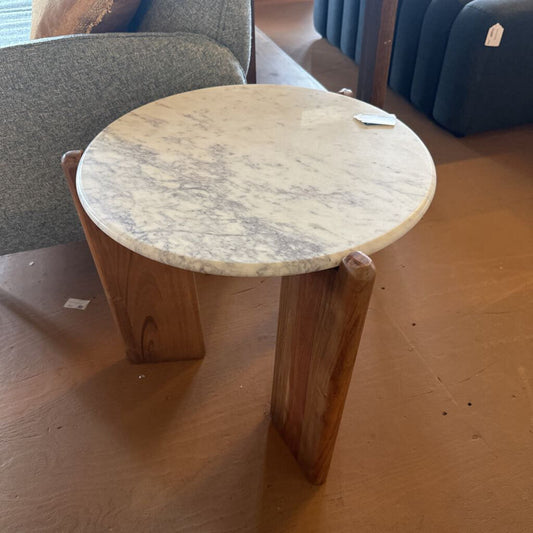 Small round table with marble-like top and wooden legs on a wooden floor.