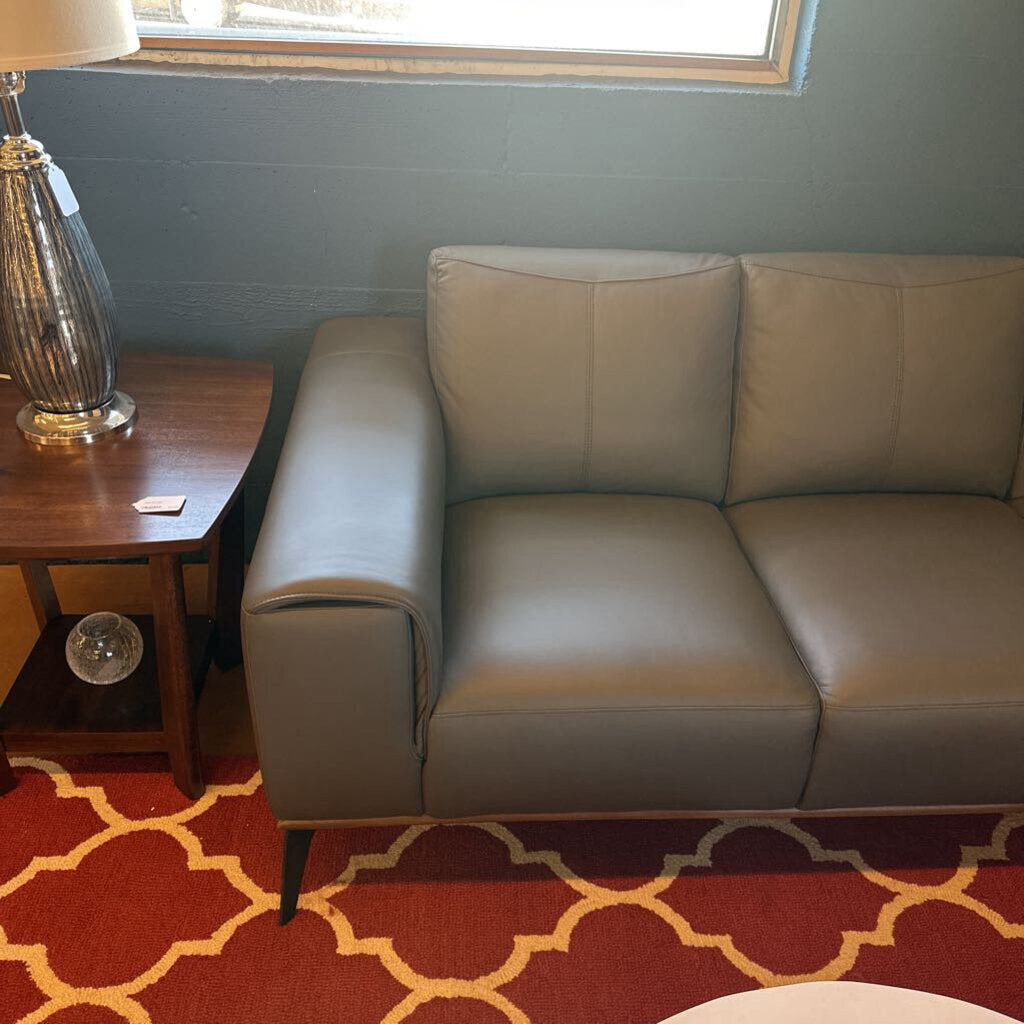 Beige leather sofa in a room with a red and yellow patterned rug, wooden side table, and lamp.