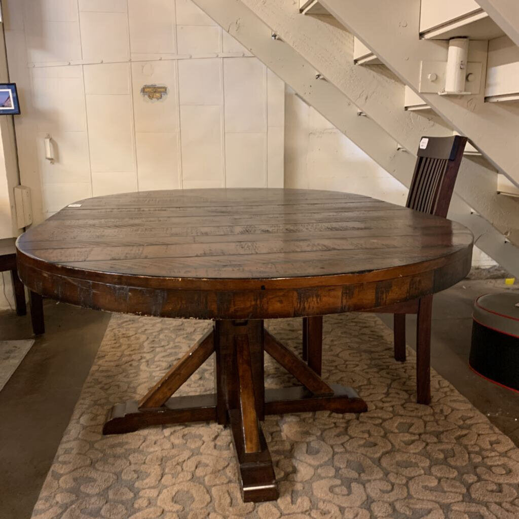 Round wooden table under a staircase in a room with tiled walls.