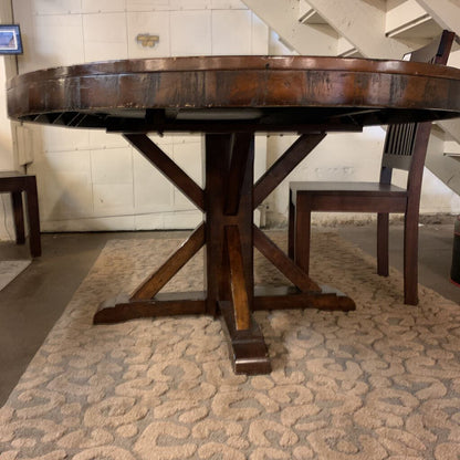 Wooden round table with a X-shaped base in a room with a patterned rug.