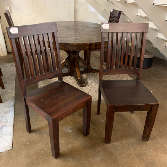 Two wooden chairs in front of a round wooden table on a concrete floor.