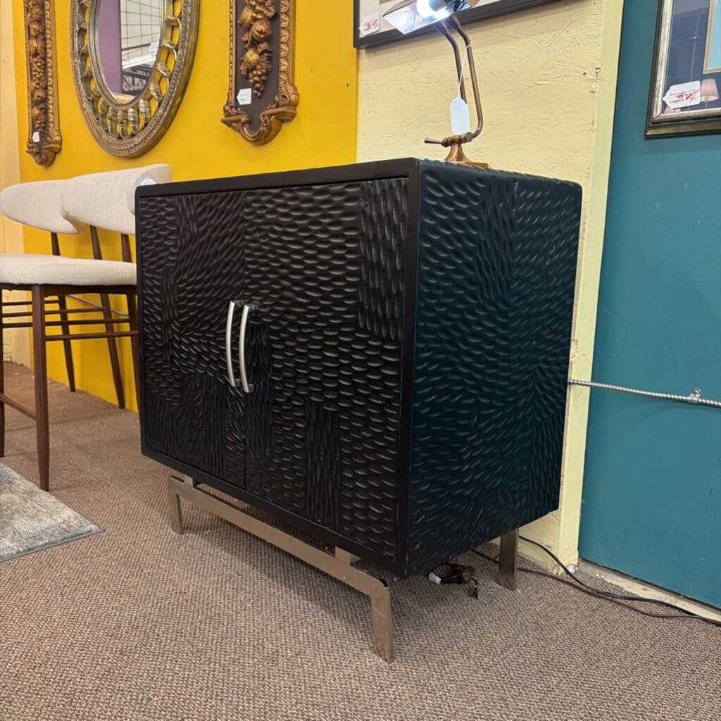 Black textured cabinet with wicker design in a room with mirrors and a chair.