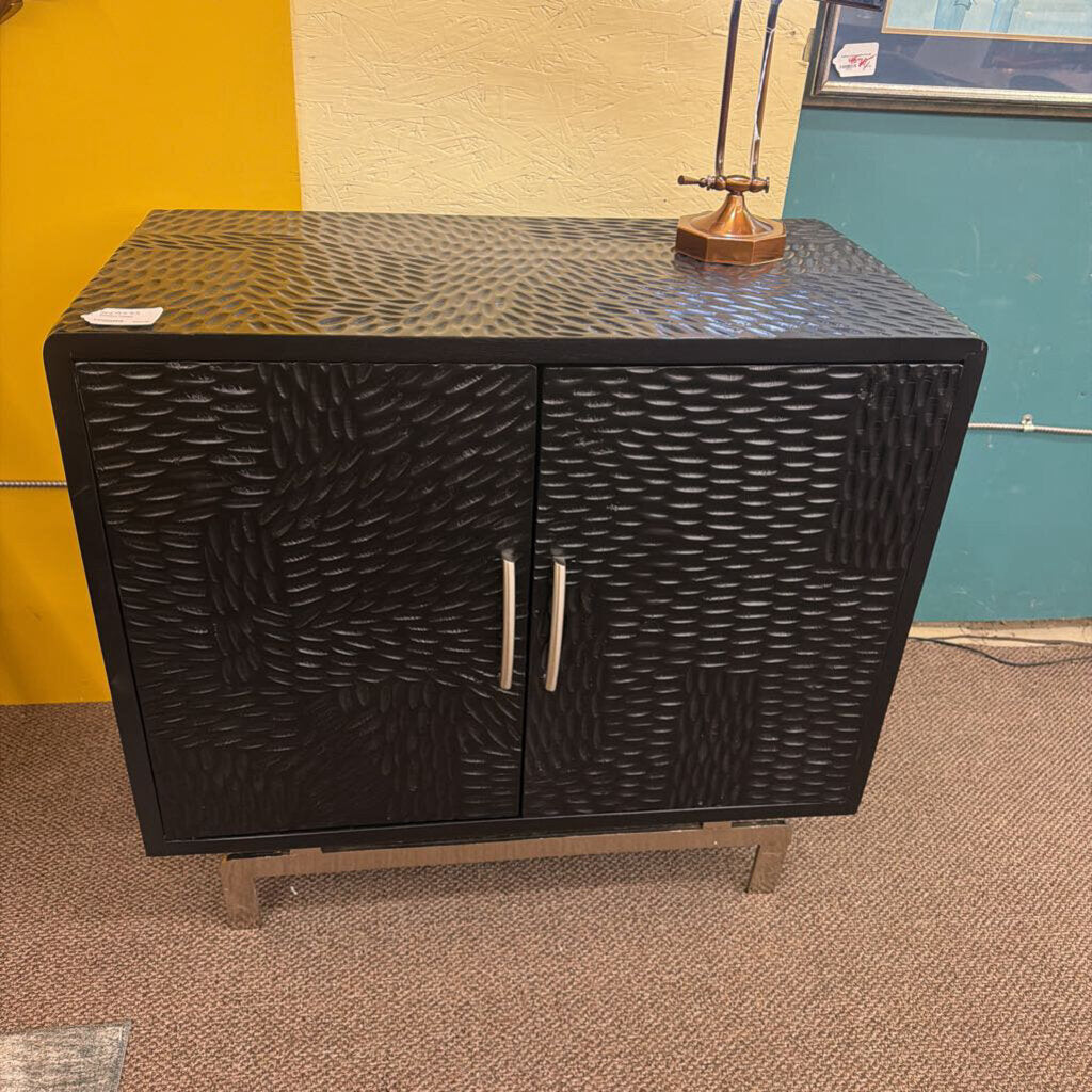 Black textured cabinet with two doors against a colorful wall.