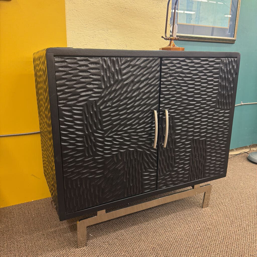 Black textured cabinet with wavy pattern on doors against a yellow wall.