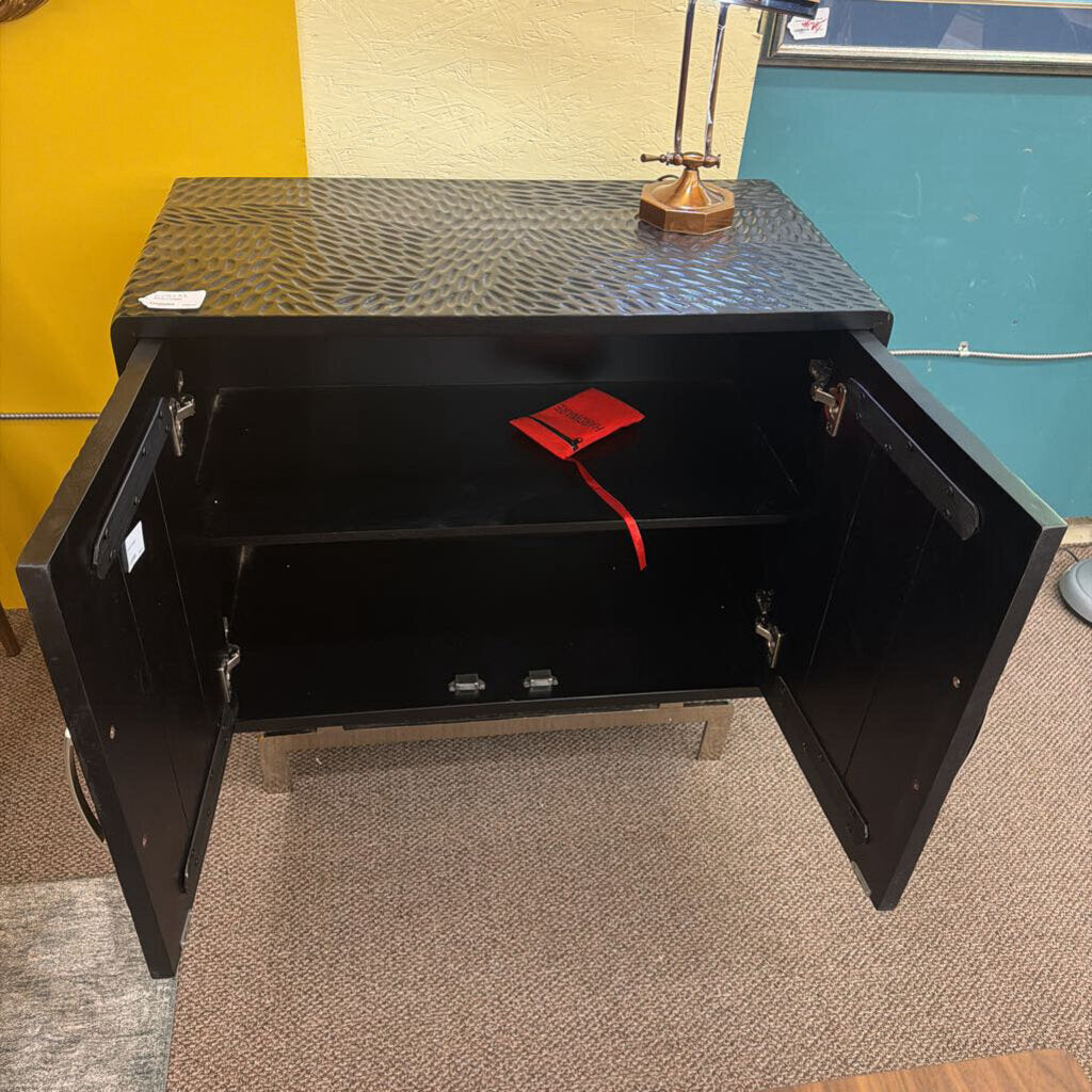 Black metal toolbox with open lid on a carpeted floor against a multicolored wall.