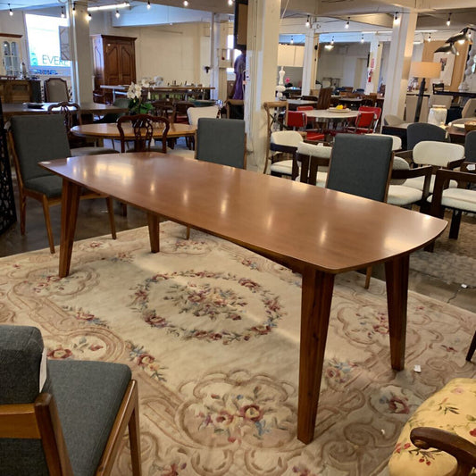 Wooden dining table with chairs on a patterned rug in a furniture store.