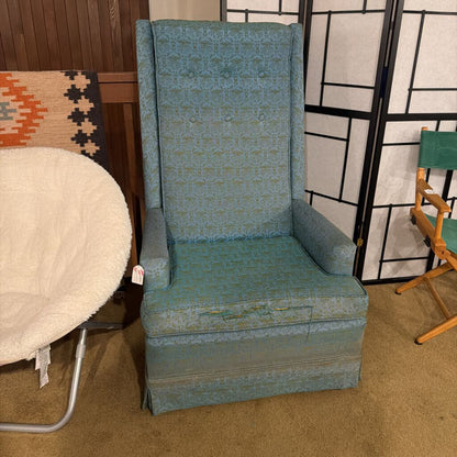 Blue upholstered chair in a room with a patterned rug and wooden furniture.