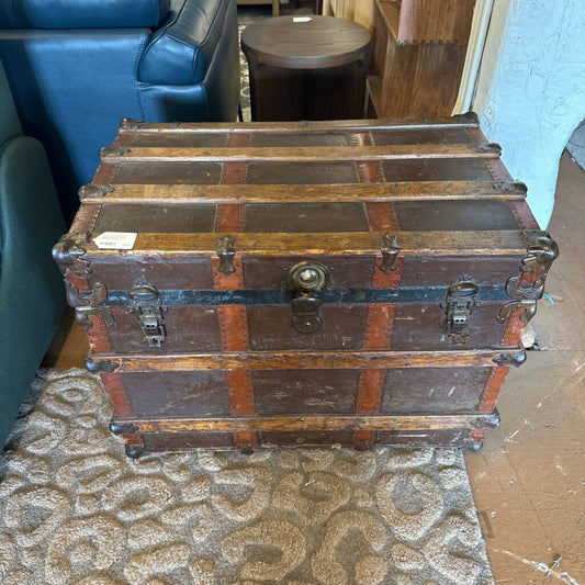 Stacked wooden trunks on a patterned rug with a blue chair and wooden stool in the background.