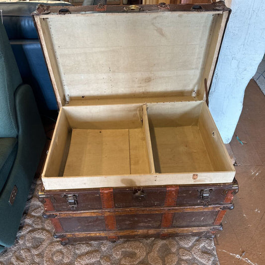 Open vintage wooden trunk on a carpeted floor with a blue wall in the background.