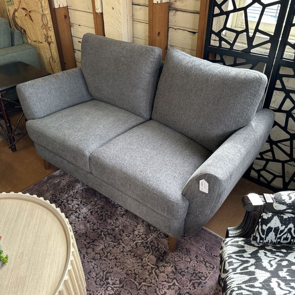Gray sofa in a room with wooden walls and a patterned rug.