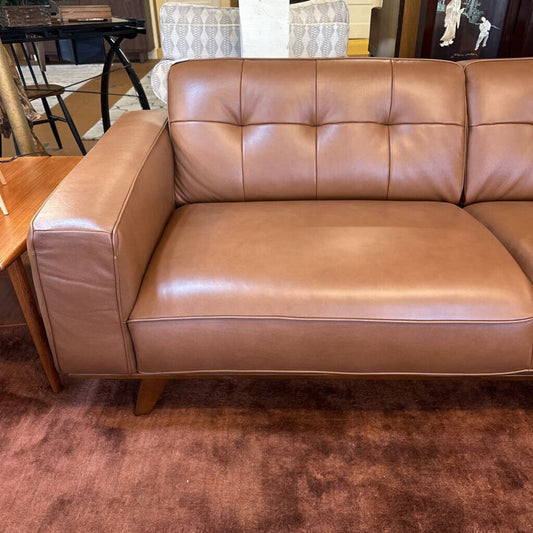 Brown leather sofa in a room with a wooden table and chairs.