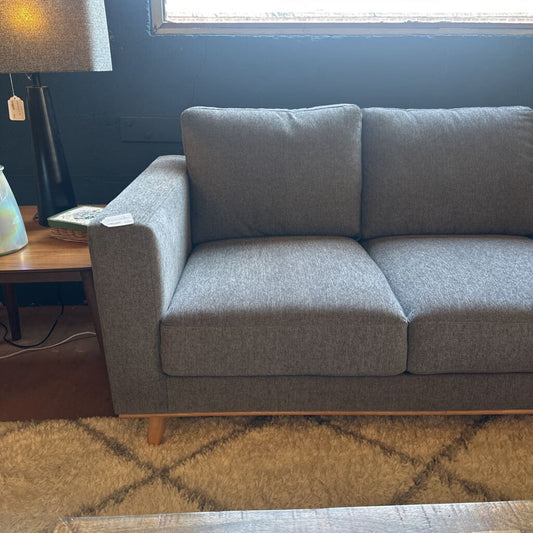 Gray sofa in a living room with a lamp and table in the background.