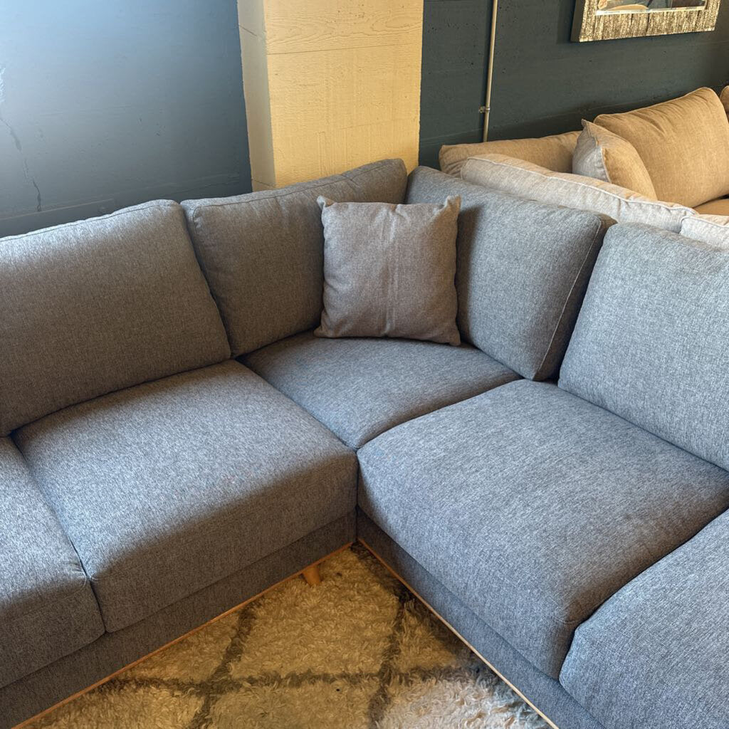 Gray sectional sofa with cushions in a room with a dark wall and light-colored floor.