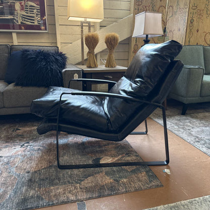 Black leather recliner chair in a living room setting with a couch and lamps.