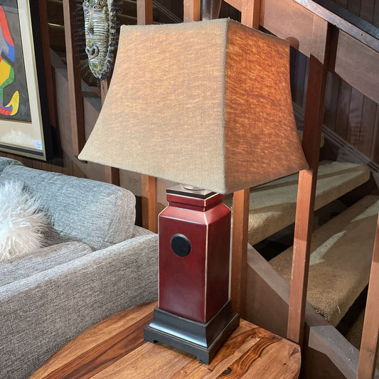 Table lamp with a wooden base and beige shade on a wooden table next to a staircase.