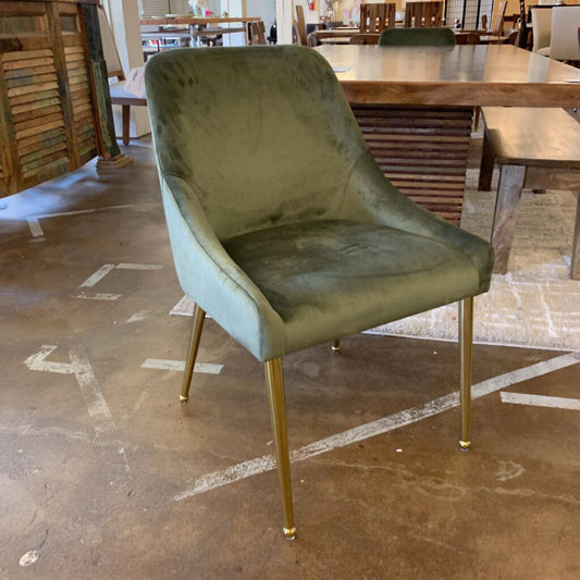 Green velvet chair with gold legs on a brown floor.