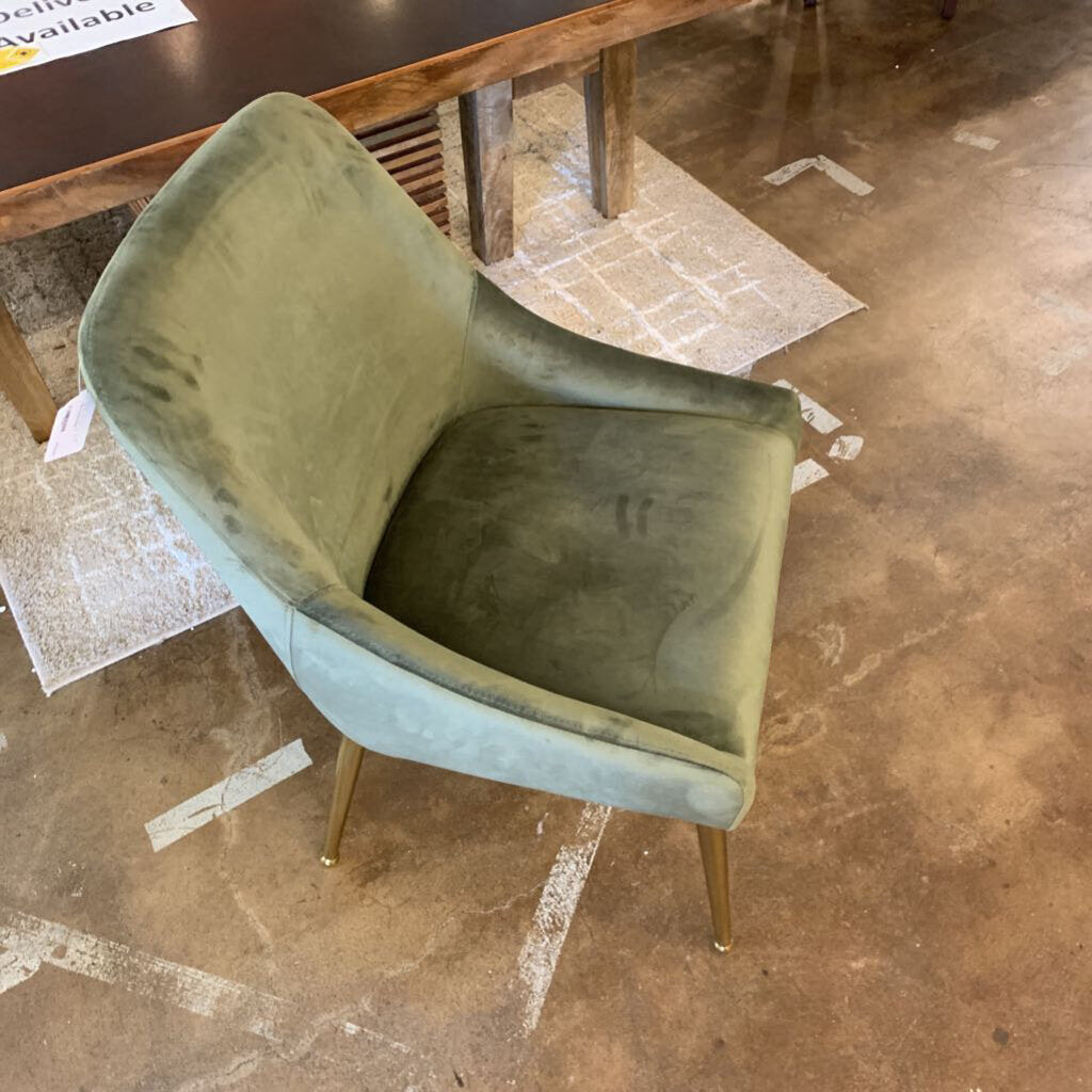 Green velvet chair with gold legs on a brown tiled floor.