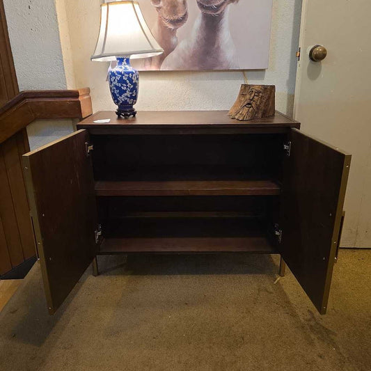 Wooden cabinet with open doors on a carpeted floor, with a lamp and decor items on top.