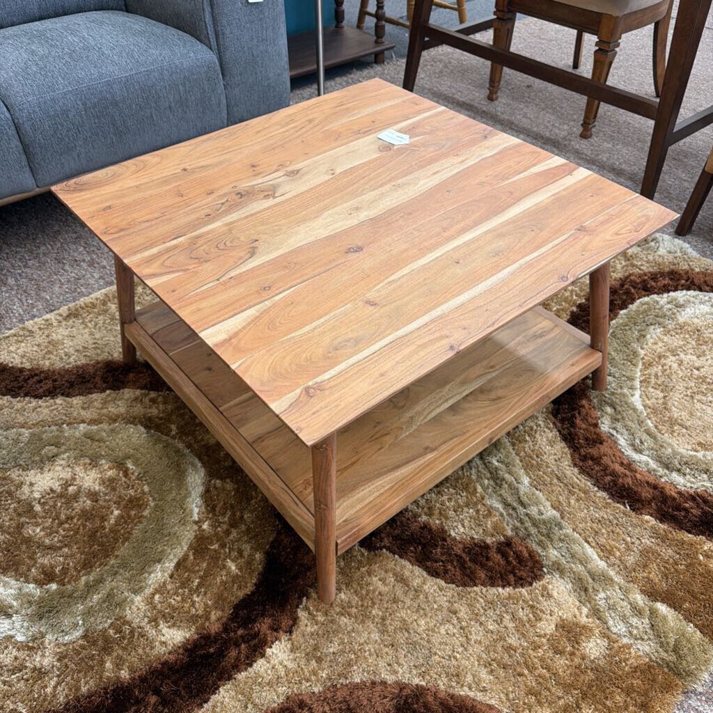 Wooden coffee table on a patterned rug with a blue sofa and wooden chairs in the background.
