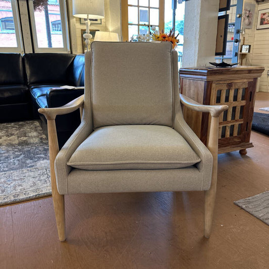 Beige armchair in a living room setting with a black sofa and wooden cabinet.