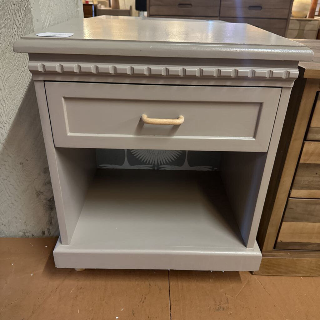 Small gray nightstand with a drawer and open shelf on a wooden floor.