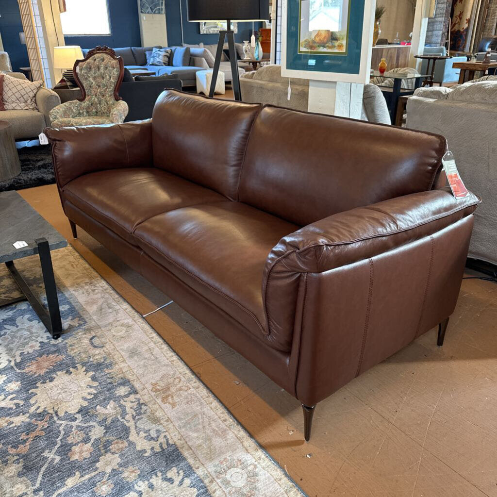 Brown leather sofa in a showroom setting with other furniture and decor.