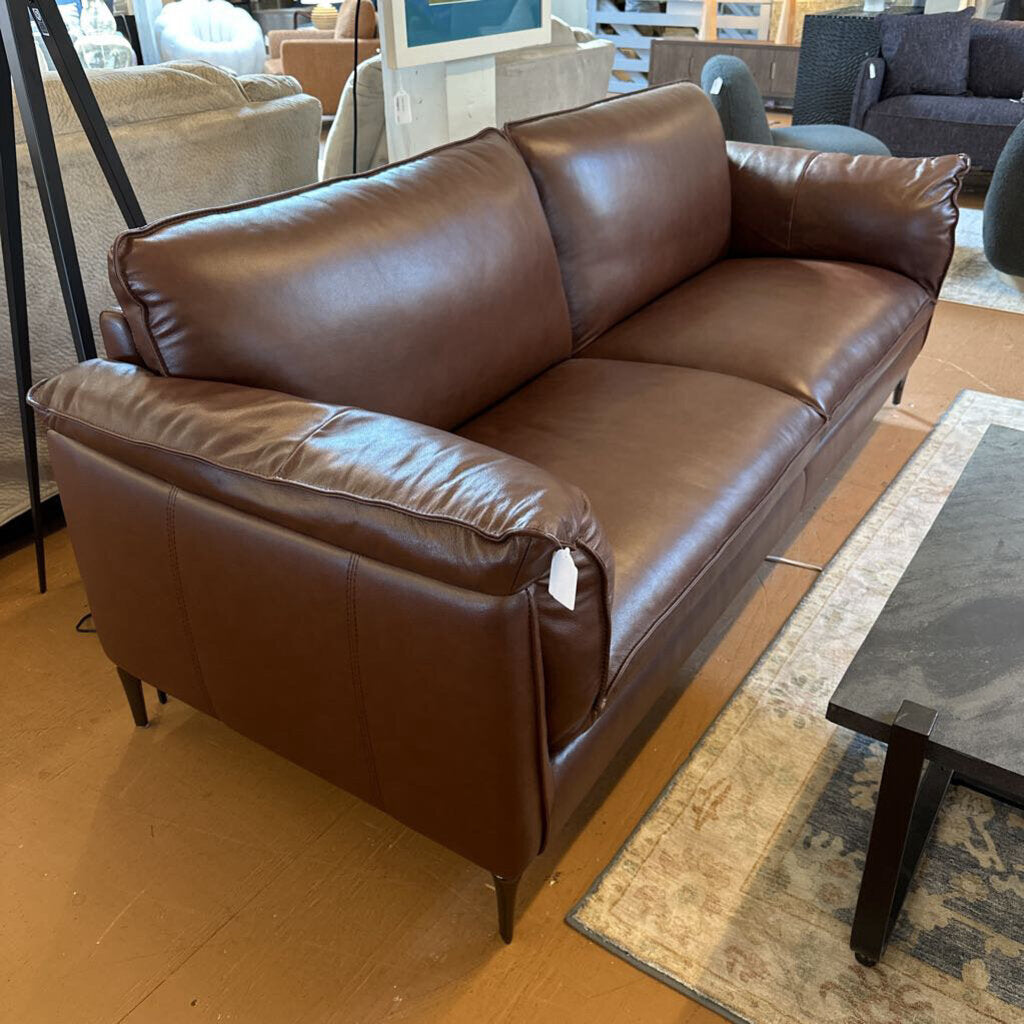 Brown leather sofa in a showroom setting with other furniture.