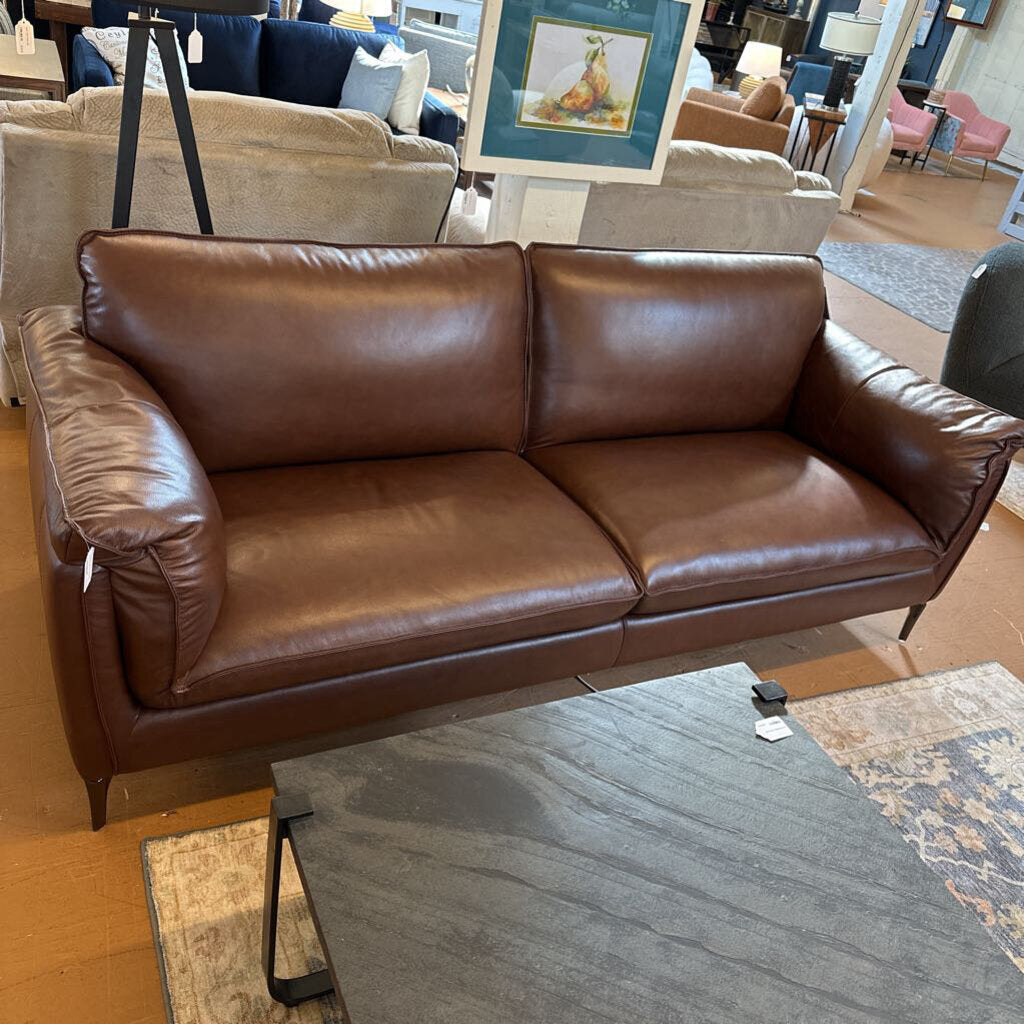 Brown leather sofa in a showroom setting with other furniture and decor.