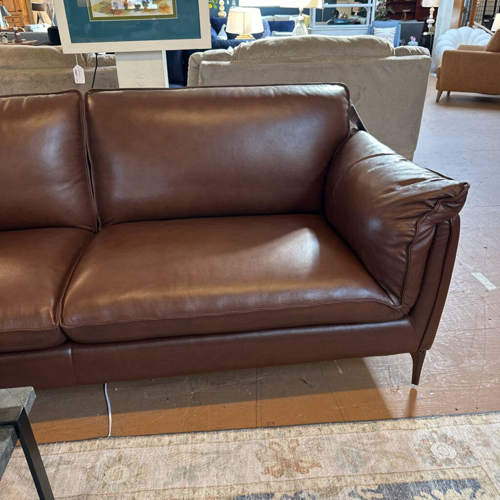 Brown leather sofa in a showroom setting with other furniture and decor.