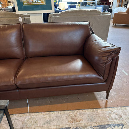 Brown leather sofa in a showroom setting with other furniture and decor.