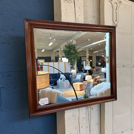 Wooden-framed mirror reflecting a room with furniture and decor.