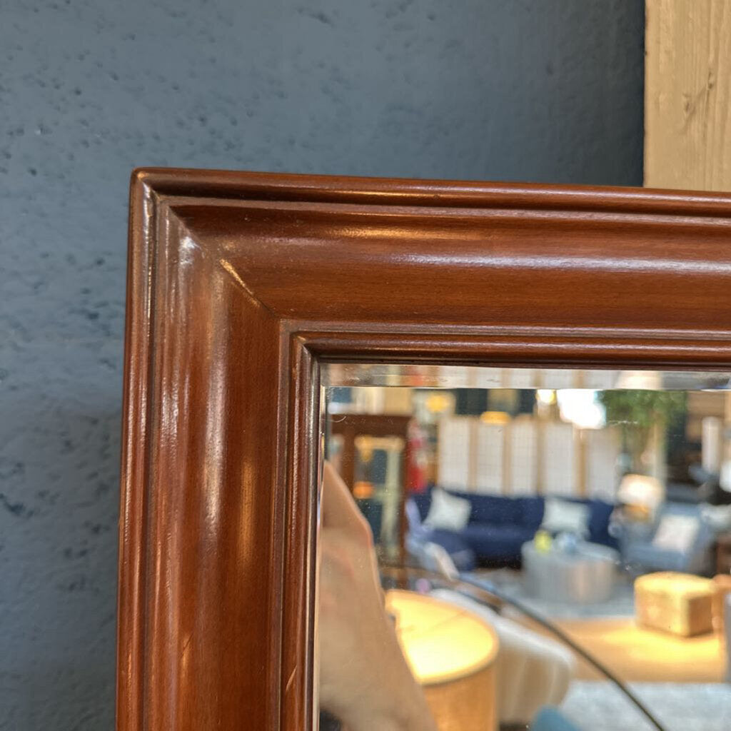 Wooden-framed mirror reflecting a room with furniture
