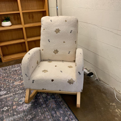 Rustic rocking chair with floral pattern on a carpeted floor next to a wooden bookshelf.