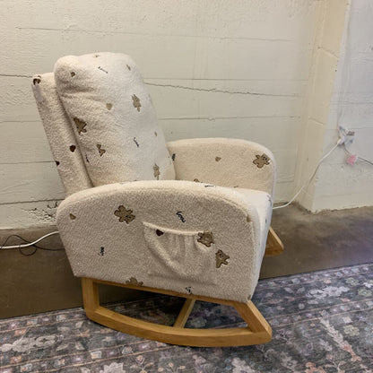 Beige rocking chair with floral patterns on a textured floor and light-colored wall.