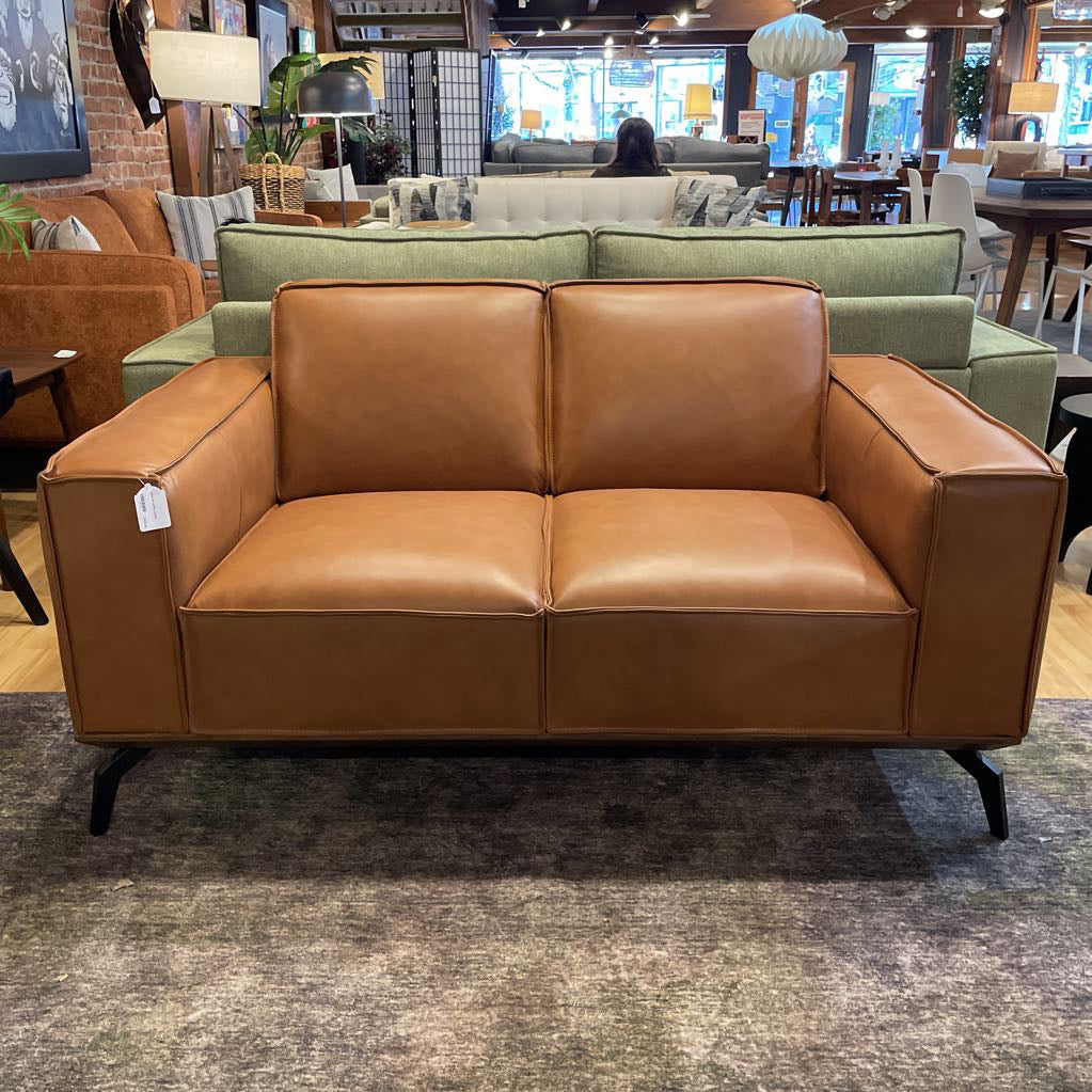 Brown leather sofa in a showroom with other furniture in the background