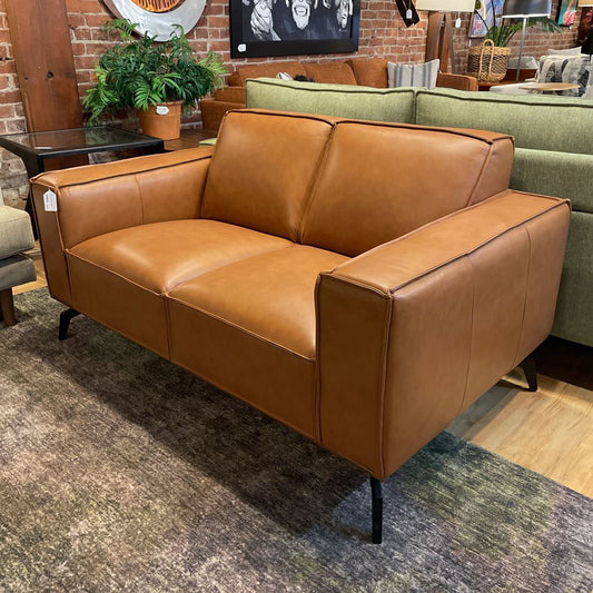 Brown leather sofa in a showroom setting with other furniture and decor items.