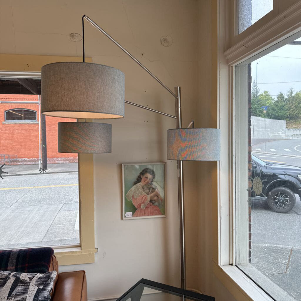Modern floor lamp with two gray lampshades in a room with large windows.