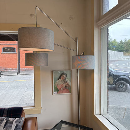 Modern floor lamp with two gray lampshades in a room with large windows.