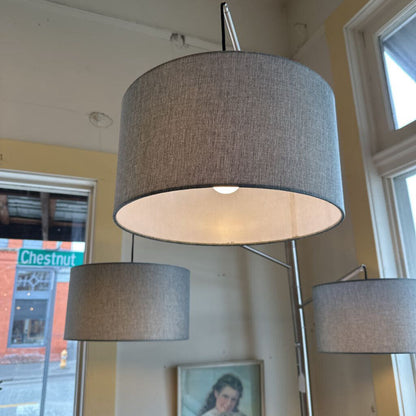 Floor lamp with three gray lampshades in a room with windows and a picture on the wall.