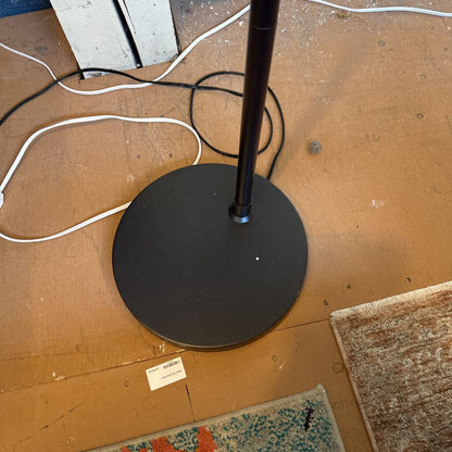 Black floor lamp base on a wooden floor with visible brand label