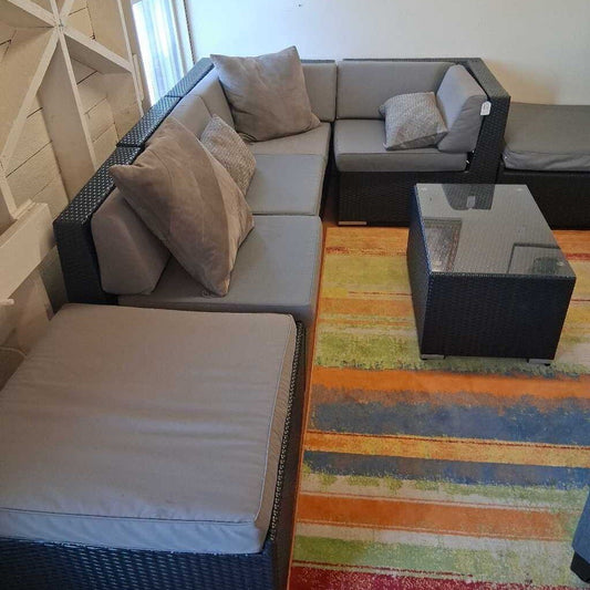 Gray sectional sofa with cushions on a colorful striped rug in a room with wooden walls.