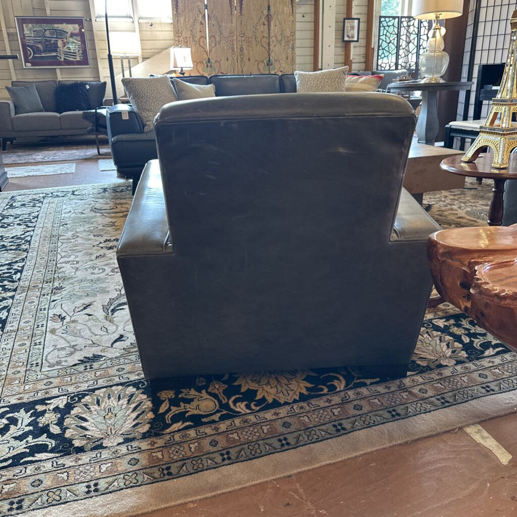 Dark leather armchair in a living room setting with a patterned rug and furniture.