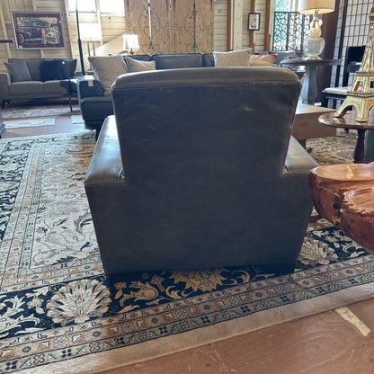 Dark leather armchair in a living room setting with a patterned rug and furniture.