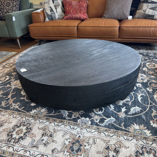 Round dark wood coffee table on a patterned rug with a brown sofa in the background.