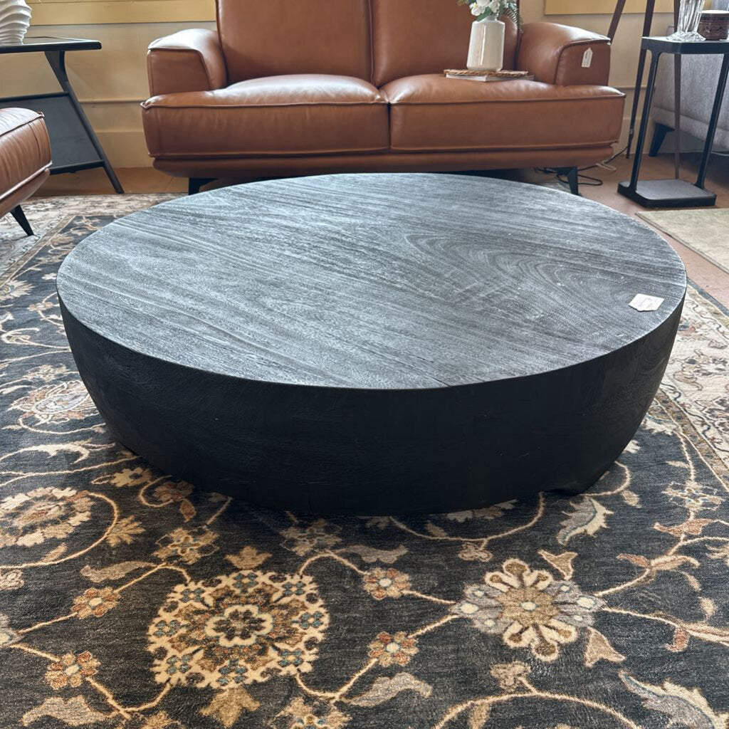 Round black marble coffee table in a living room setting with a brown leather sofa.
