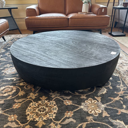 Round black marble coffee table in a living room setting with a brown leather sofa.