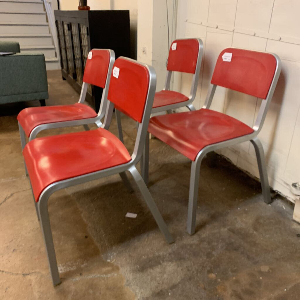 Four red chairs with metal frames on a concrete floor.