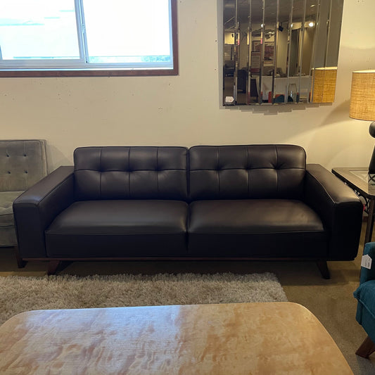 Black leather sofa in a room with a mirror and window.