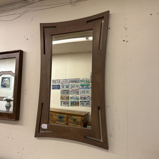 Wooden-framed mirror on a wall with visible license plates in the reflection