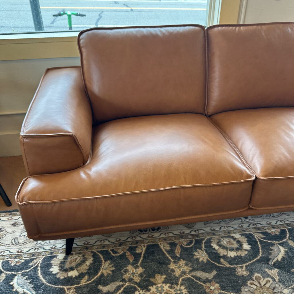 Brown leather sofa in a room with a window and rug.